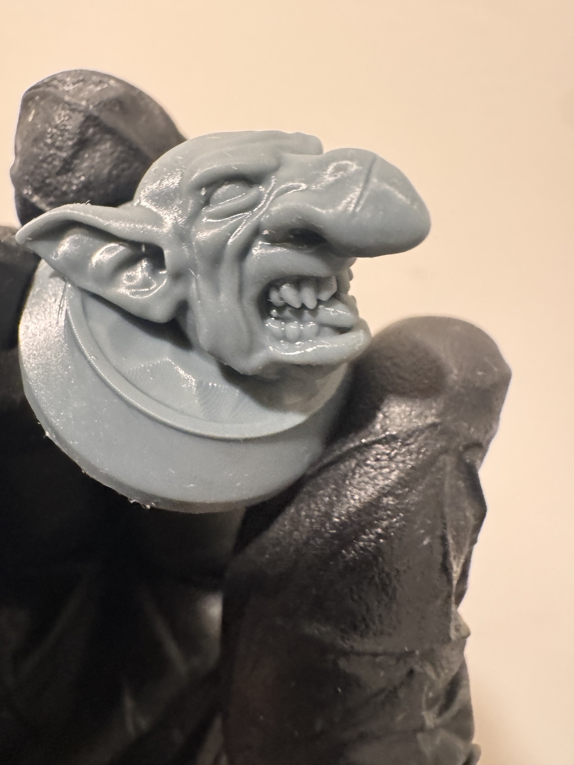 Close-up of an unpainted goblin paint topper held in a gloved hand