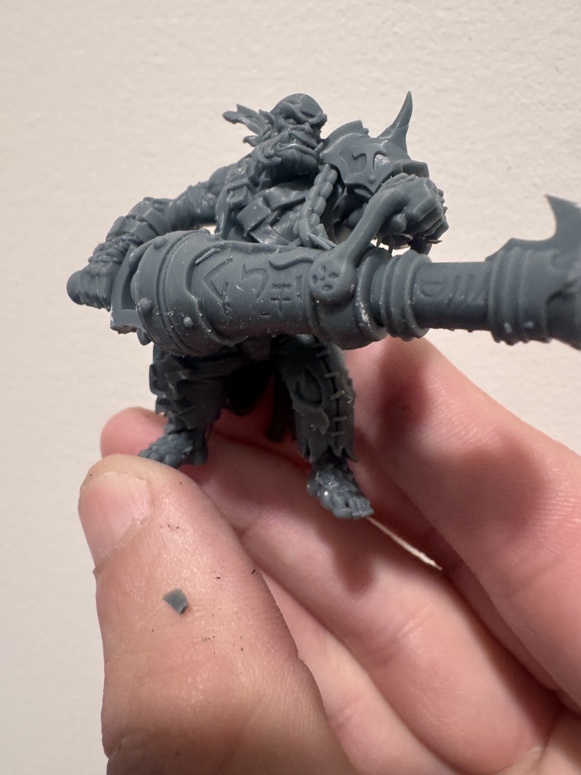 Unpainted Dread Armada model holding a large cannon, held between fingers for scale